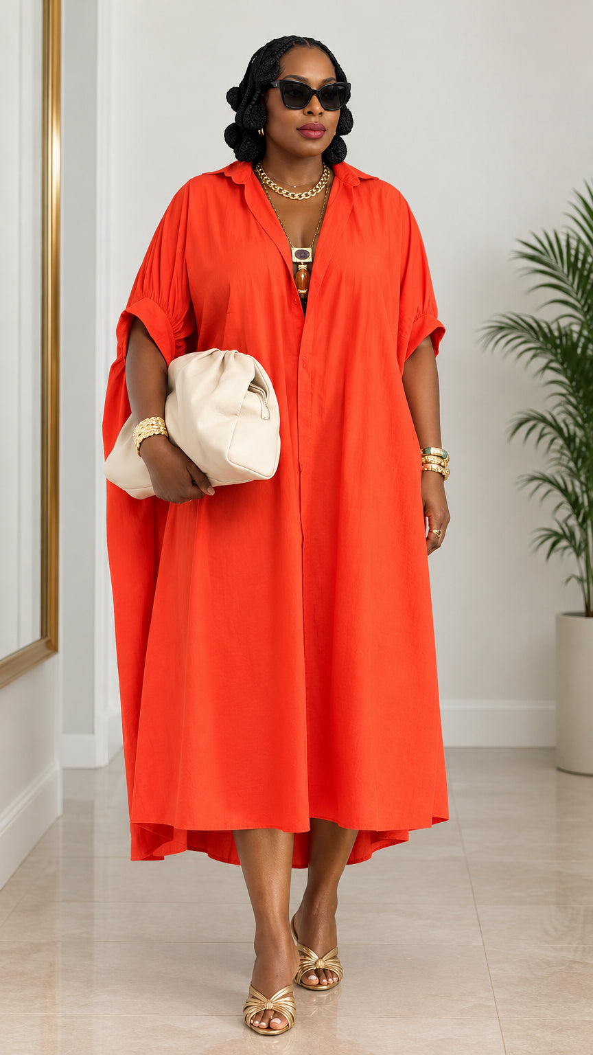 Front view of woman wearing orange oversized kaftan shirt dress with sunglasses and cream clutch