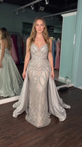 Model wearing silver sequined mermaid evening gown with dramatic detachable overskirt, front view