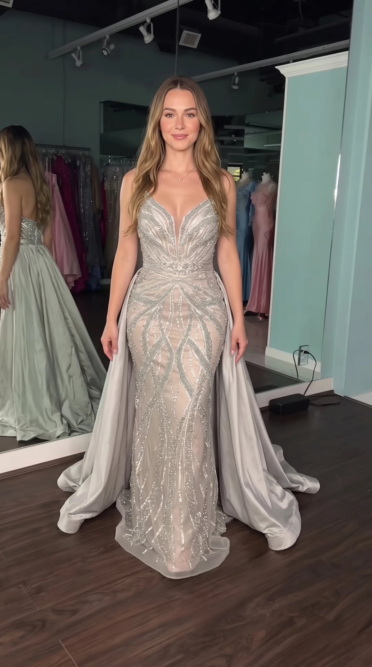 Model wearing silver sequined mermaid evening gown with dramatic detachable overskirt, front view