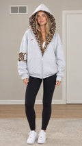 Front view of woman wearing Light Grey zip-up hoodie with leopard lined hood and black leggings