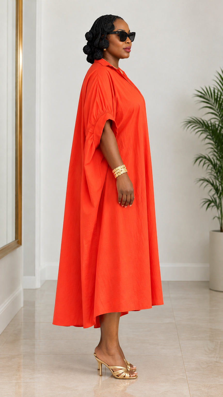 Side profile view of woman wearing draped orange midi shirt dress with gold heels