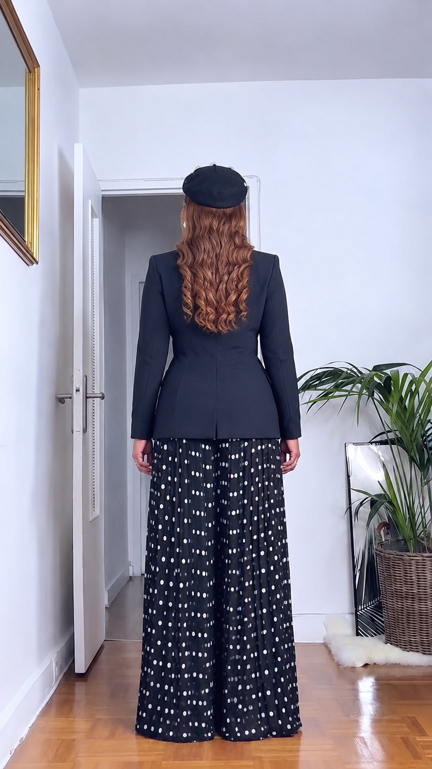 Back view of woman wearing black tailored jacket and polka dot pleated wide leg trousers