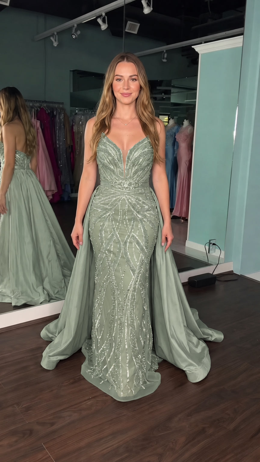 Model wearing sage green beaded formal gown with matching detachable dramatic overskirt