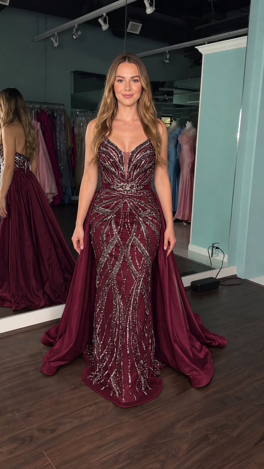 Model wearing deep burgundy sequined mermaid formal dress featuring detachable full overskirt