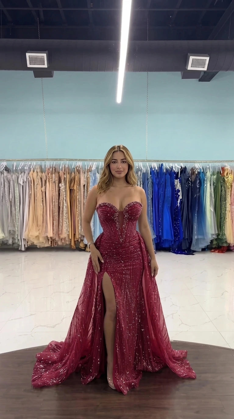 Front view of woman wearing burgundy strapless corset evening gown with beading and slit